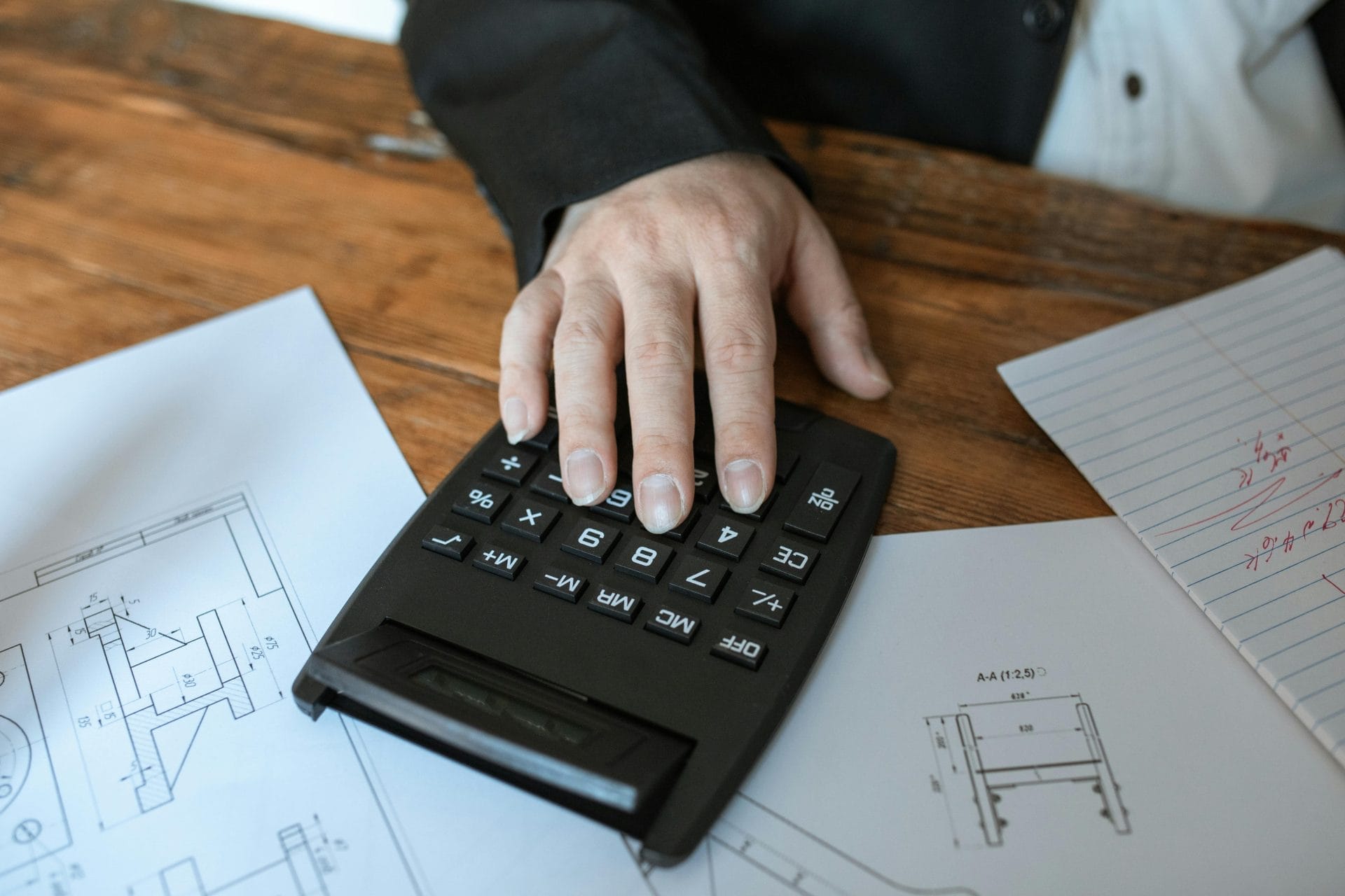 Hand using calculator for architectural calculations on blueprints.