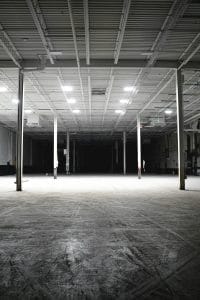Explore the vast and empty interior of an industrial warehouse with bright overhead lights.