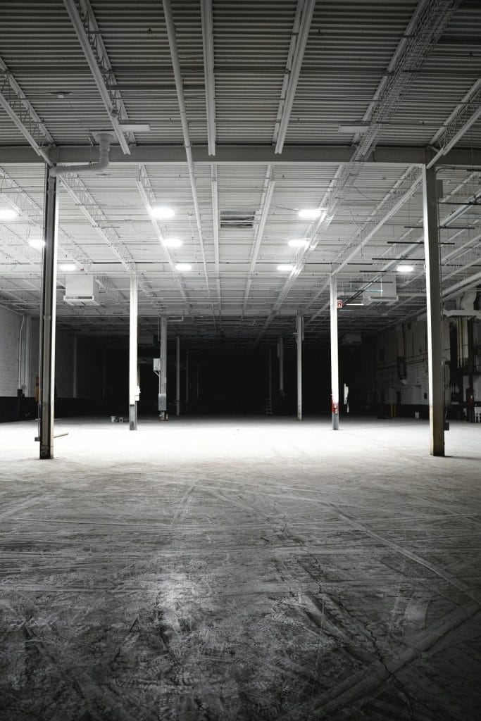Explore the vast and empty interior of an industrial warehouse with bright overhead lights.