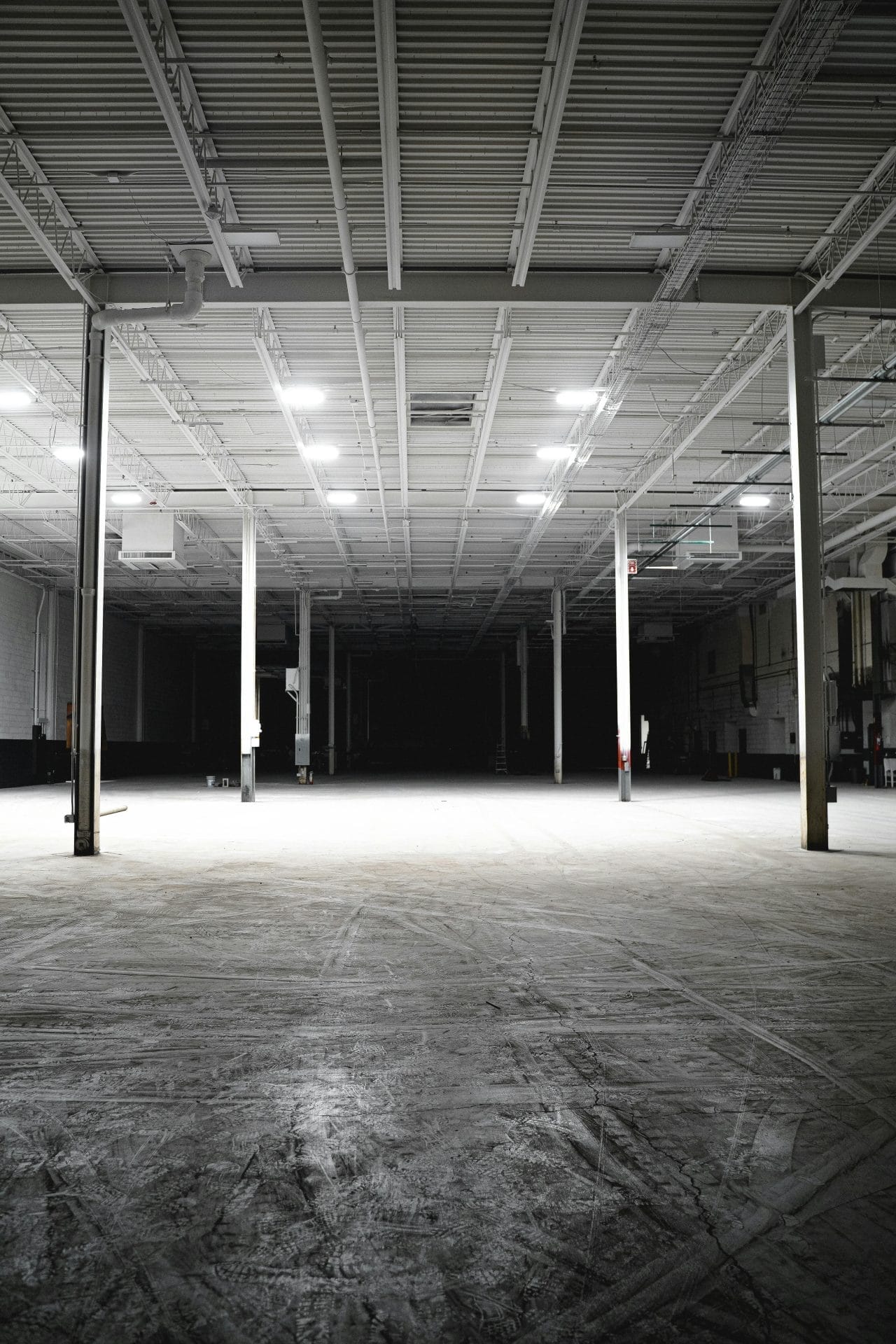 Explore the vast and empty interior of an industrial warehouse with bright overhead lights.